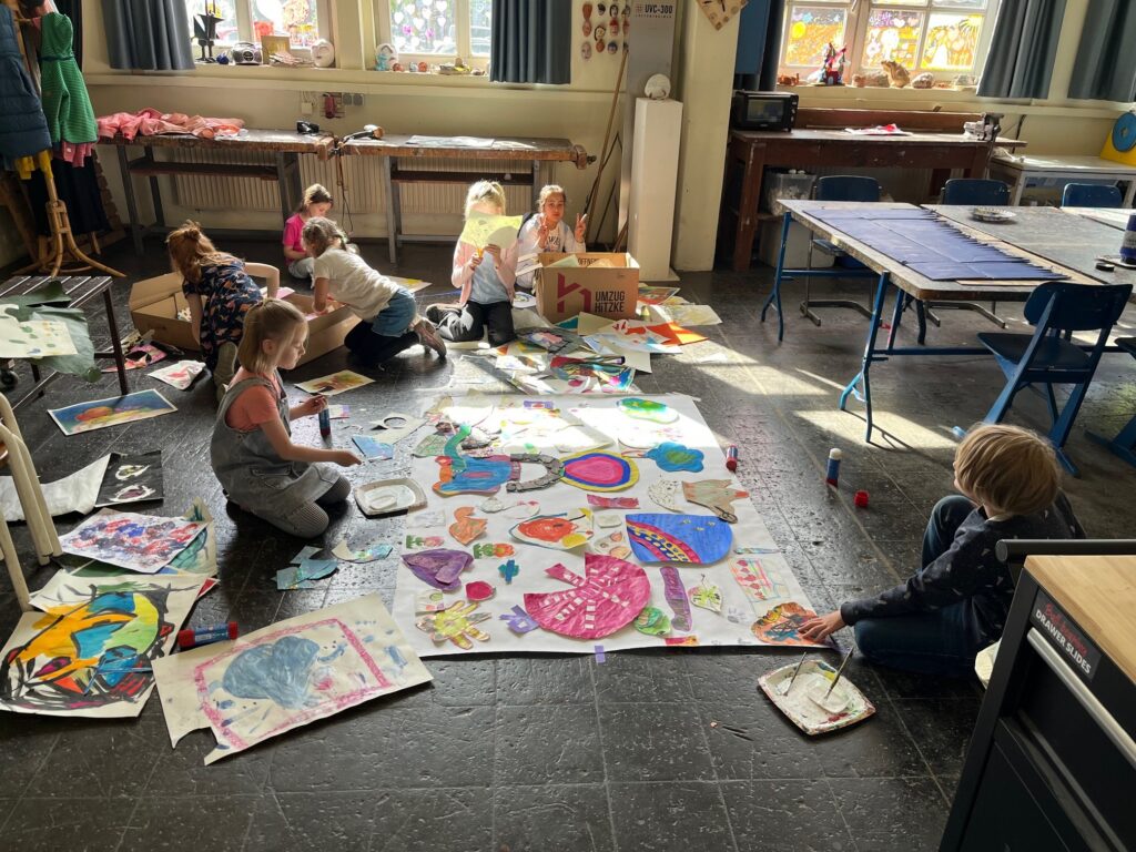 Kinder sitzen auf dem Boden mit großem Papier und erschaffen Kunstwerke